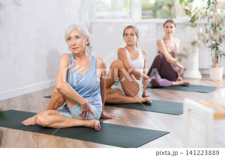 Portrait of women different ages practicing Matsyendrasana known as Lord of Fishes Pose during group yoga training in studio Portrait of women different ages practicing Matsyendrasana known as Lord of Fishes Pose during group yoga training in studio 141223889