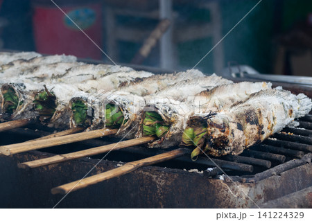 Traditional salt crusted grilled fish stuffed fresh herbs roasting over charcoal smoky aroma rustic cooking style authentic local street food presentation 141224329