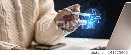 A close-up of a person wearing a knit sweater interacting with a holographic quantum processor chip interface using a digital stylus pen, representing advanced technology, AI, and computing 141225406