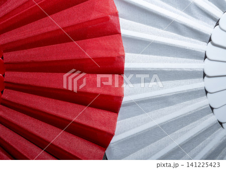A close-up macro photograph highlighting the contrasting textures and vibrant colors of red and white fabric pleated folds on a handheld fan, creating an abstract geometric pattern A close-up macro photograph highlighting the contrasting textures and vibrant colors of red and white fabric pleated folds on a handheld fan, creating an abstract geometric pattern 141225423