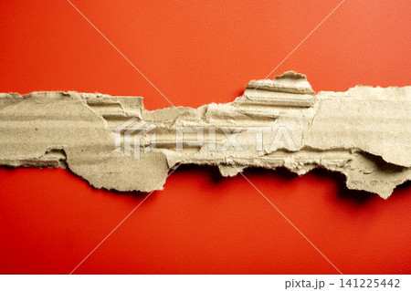 Ripped and torn strip of corrugated brown cardboard showing its internal texture, set against a vibrant, bright red paper background. Great for copy space or texture Ripped and torn strip of corrugated brown cardboard showing its internal texture, set against a vibrant, bright red paper background. Great for copy space or texture 141225442