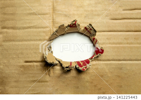 A ragged, circular hole torn through a brown corrugated cardboard sheet, revealing an empty white background. Perfect for framing messages, copy space, or design concepts A ragged, circular hole torn through a brown corrugated cardboard sheet, revealing an empty white background. Perfect for framing messages, copy space, or design concepts 141225443
