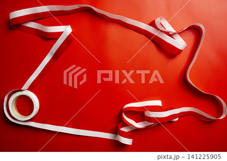 A close-up of a roll of red and white striped ribbon elegantly unwound and spread across a vibrant red paper background, perfect for holidays, gift wrapping, or festive crafts A close-up of a roll of red and white striped ribbon elegantly unwound and spread across a vibrant red paper background, perfect for holidays, gift wrapping, or festive crafts 141225905