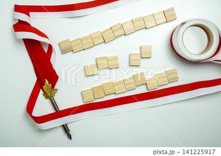 Red and white ribbon, blank wooden tiles, ribbon roll, and pen on white background. Perfect for patriotic or festive copy space Red and white ribbon, blank wooden tiles, ribbon roll, and pen on white background. Perfect for patriotic or festive copy space 141225917