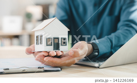 Real estate contract for property mortgage finance approved, home insurance document protects homeowner and house tenant, investment strategy involves agent holding model house near laptop Real estate contract for property mortgage finance approved, home insurance document protects homeowner and house tenant, investment strategy involves agent holding model house near laptop 141226169