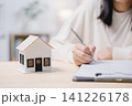 Close up of woman hand writing estate property residential investment agreement, signing domestic construction insurance mortgage contract with small house model on table 141226178