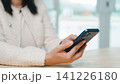 Woman uses mobile phone, smartphone technology online to connect, as she sits at wooden table wearing white textured jacket to browse social media or text friends in bright office space 141226180