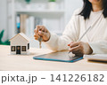 Woman signs digital contract for real estate purchase on tablet while holding house key near miniature home model, representing mortgage approval and property investment 141226182