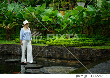 Woman walks on stones in a garden with green plants 141226307