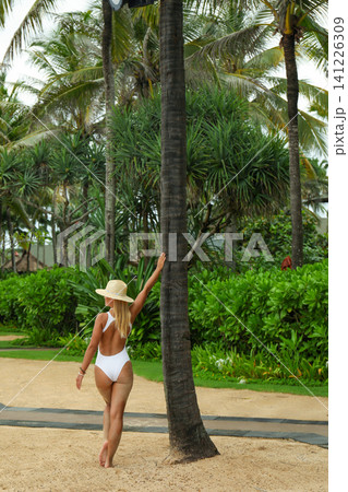 Woman walks on sandy path with palm trees in Bali Woman walks on sandy path with palm trees in Bali 141226309