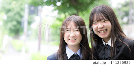 屋外の緑背景で笑顔で寄り添う日本人女子高校生 二人で過ごす高校生活と青春 カメラ目線笑顔 屋外の緑背景で笑顔で寄り添う日本人女子高校生 二人で過ごす高校生活と青春 カメラ目線笑顔 141226923