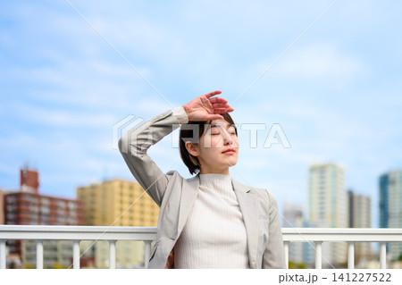 日差しを避け額に手を当てる女性 141227522