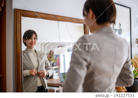 鏡の前でジャケットのボタンを留める女性 鏡の前でジャケットのボタンを留める女性 141227531