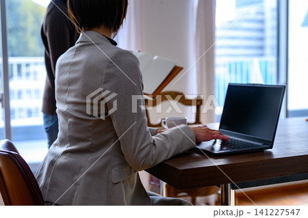 オフィスでノートパソコンを操作する女性の後ろ姿と資料を持つ女性 オフィスでノートパソコンを操作する女性の後ろ姿と資料を持つ女性 141227547
