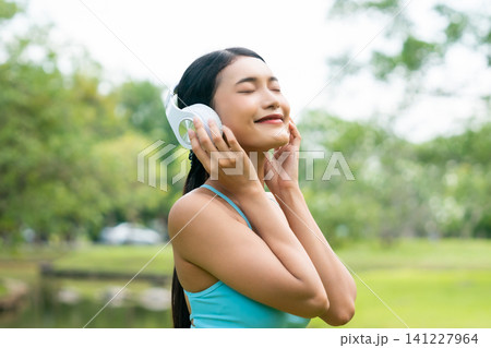 Asian sports woman listening to music on headphones outdoors Asian sports woman listening to music on headphones outdoors 141227964