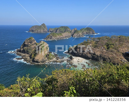 A breathtaking high-angle ocean view from a wooden viewpoint structure, showcasing lush green rocky islets scattered across the vibrant blue sea under the clear sky on a sunny summer day in Indonesia. A breathtaking high-angle ocean view from a wooden viewpoint structure, showcasing lush green rocky islets scattered across the vibrant blue sea under the clear sky on a sunny summer day in Indonesia. 141228356