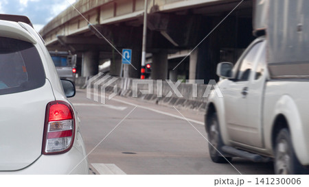 Rear view of white vehicle stationary on a road next to an elevated concrete highway structure. Traffic is visible in the lane during a bright sunny daytime environment. Fast speed of pickup car. 141230006