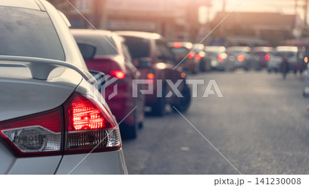 Rear view shot of a silver car waiting in heavy city traffic during the day. The bright red tail light is highlighted as multiple vehicles queue up on the road creating a busy commute scene. Rear view shot of a silver car waiting in heavy city traffic during the day. The bright red tail light is highlighted as multiple vehicles queue up on the road creating a busy commute scene. 141230008