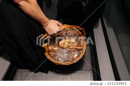 Top view of a woman holding a wicker basket filled with decorated Halloween cookies wrapped in transparent gift bags while riding an escalator. Seasonal treats, festive shopping and holiday Top view of a woman holding a wicker basket filled with decorated Halloween cookies wrapped in transparent gift bags while riding an escalator. Seasonal treats, festive shopping and holiday 141230953