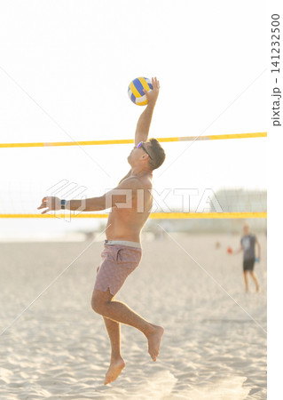 Male athlete spiking volleyball during beach game Male athlete spiking volleyball during beach game 141232500