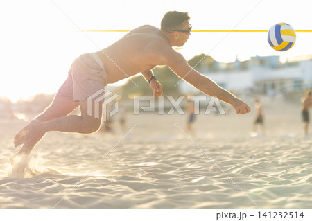 Man diving for volleyball on sandy beach at sunset Man diving for volleyball on sandy beach at sunset 141232514