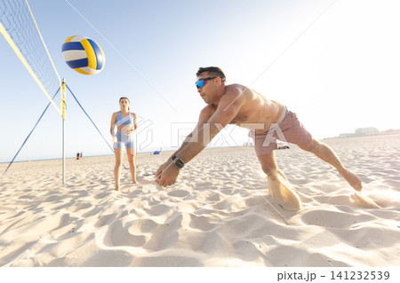 Man diving for beach volleyball on summer day Man diving for beach volleyball on summer day 141232539
