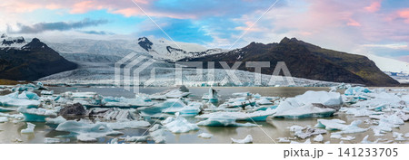 Panoramic view of Glacier Lagoon and Glacier in southeast Iceland, with floating icebergs, rugged mountains, and colorful skies creating a breathtaking Arctic landscape. 141233705