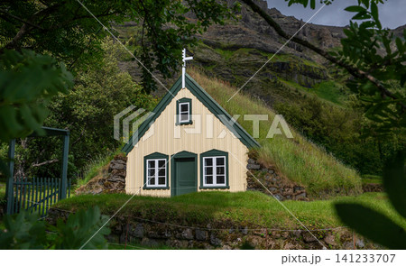 Historic Hofskirkja turf church surrounded by lush greenery beneath Icelandic mountains. One of the country's last traditional turf churches, blending architecture with nature. Historic Hofskirkja turf church surrounded by lush greenery beneath Icelandic mountains. One of the country's last traditional turf churches, blending architecture with nature. 141233707