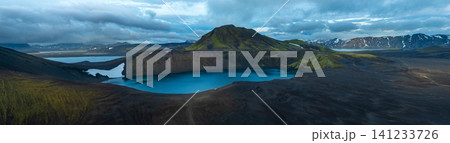 Panoramic view of crater lake in Iceland's Highlands, surrounded by dark volcanic slopes beneath dramatic storm clouds. A remote and breathtaking volcanic landscape. Panoramic view of crater lake in Iceland's Highlands, surrounded by dark volcanic slopes beneath dramatic storm clouds. A remote and breathtaking volcanic landscape. 141233726