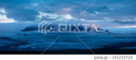 Panoramic view of a vast Icelandic glacier beneath dramatic storm clouds, with rugged volcanic peaks emerging through mist in the remote Highlands, creating a wild and atmospheric landscape. Panoramic view of a vast Icelandic glacier beneath dramatic storm clouds, with rugged volcanic peaks emerging through mist in the remote Highlands, creating a wild and atmospheric landscape. 141233728