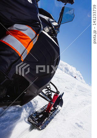 Close-up perspective of a snowmobile rider crossing a pristine Icelandic glacier, following another snowmobile across untouched snow beneath a vivid blue sky during a winter adventure. 141233739