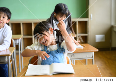 教室で勉強する女子小学生を傍で見守る男性教師 教室で勉強する女子小学生を傍で見守る男性教師 141235544