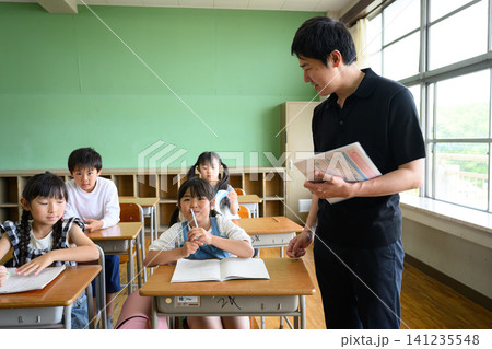 教室で勉強する女子小学生を傍で見守る男性教師 教室で勉強する女子小学生を傍で見守る男性教師 141235548