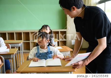 教室で勉強する女子小学生を傍で見守る男性教師 教室で勉強する女子小学生を傍で見守る男性教師 141235549
