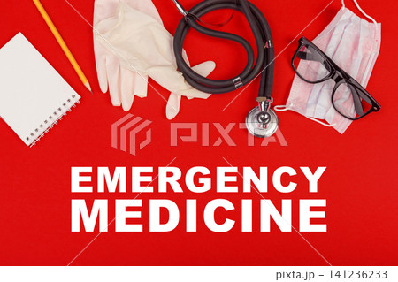 Emergency medicine tools and supplies on a red surface with a stethoscope, gloves, mask, notebook, and glasses 141236233