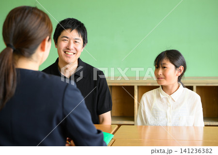 教室で笑顔で和やかに三者面談をする女性教師と父親と小学生の女の子（進路相談・学習塾） 141236382