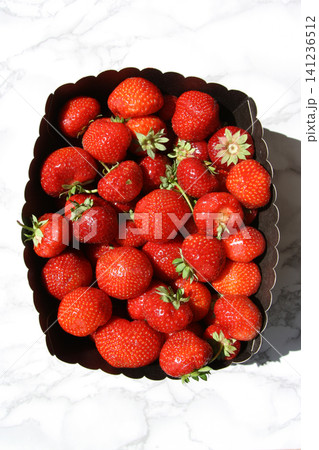 Sunlit Fresh Strawberries Packed in a Dark Scalloped Punnet on Marble Sunlit Fresh Strawberries Packed in a Dark Scalloped Punnet on Marble 141236512