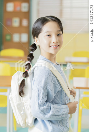 Schoolgirl with backpack smiling in a bright classroom Schoolgirl with backpack smiling in a bright classroom 141237172