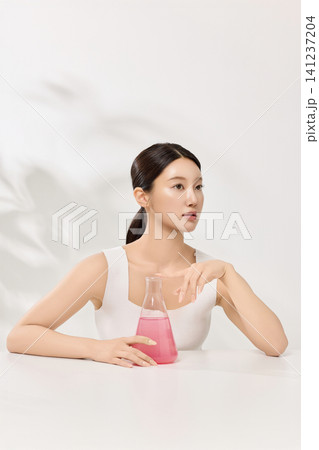 Young Asian woman presenting pink cosmetic formula in glass laboratory flasks 141237204
