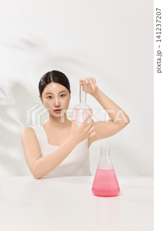 Asian woman posing with laboratory glassware and pink beauty serum 141237207