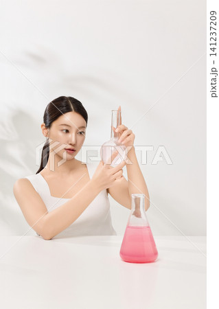 Beauty model holding beakers with pink skincare liquid in a clean studio 141237209
