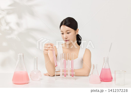 Young Asian woman presenting pink cosmetic formula in glass laboratory flasks Young Asian woman presenting pink cosmetic formula in glass laboratory flasks 141237228
