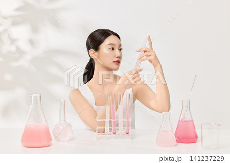 Beauty model holding beakers with pink skincare liquid in a clean studio 141237229