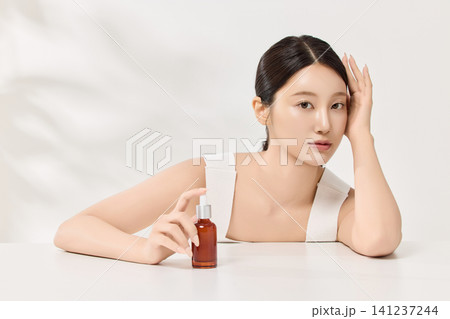 Beauty model posing with a brown cosmetic bottle in a clean studio Beauty model posing with a brown cosmetic bottle in a clean studio 141237244