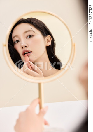 Young Asian woman applying makeup with a compact mirror 141237522