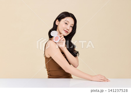 Young Asian woman applying makeup with a compact mirror Young Asian woman applying makeup with a compact mirror 141237528