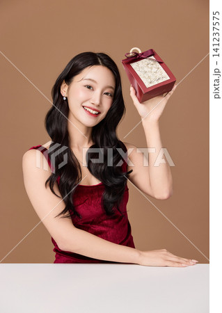 Woman in a red dress holding a decorative gift package 141237575