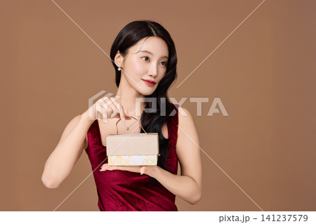Smiling woman showing a ribbon-wrapped present in a studio Smiling woman showing a ribbon-wrapped present in a studio 141237579