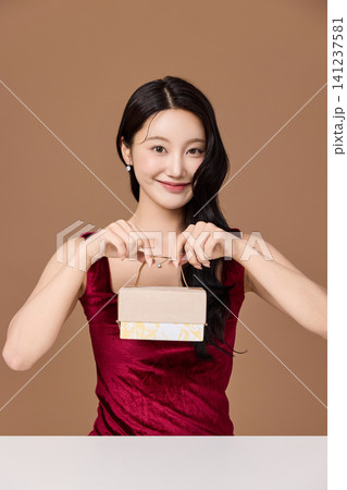 Woman in a red dress holding a decorative gift package Woman in a red dress holding a decorative gift package 141237581