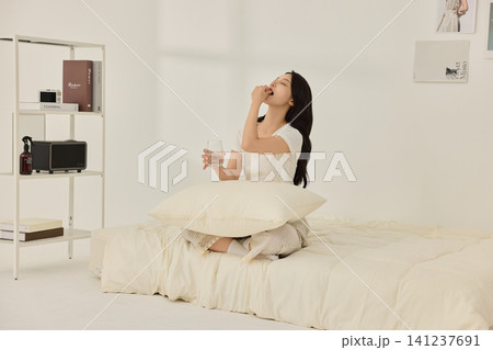 Asian woman sitting in bed with a glass of water 141237691